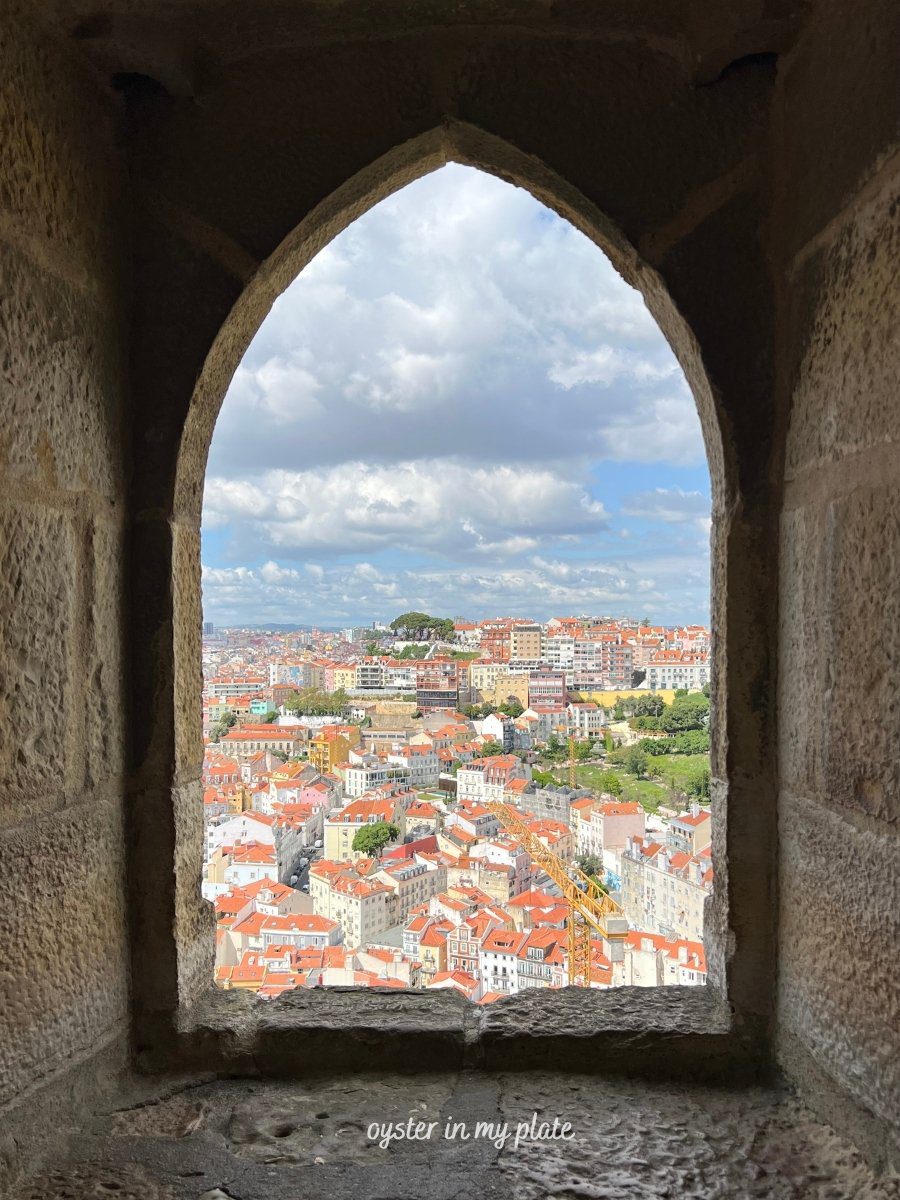 A view of Lisbon's orange rooftops and the cityscape from an arched window inside São Jorge Castle.